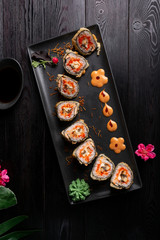 Set sushi rolls on a black rectangular plate on a dark wooden background