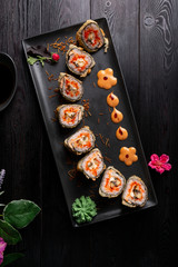 Set sushi rolls on a black rectangular plate on a dark wooden background