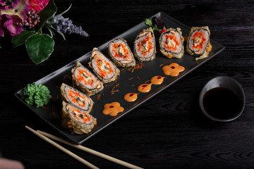 Set sushi rolls on a black rectangular plate, chopsticks and soy sauce on a dark wooden background