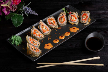 Set sushi rolls on a black rectangular plate, chopsticks and soy sauce on a dark wooden background