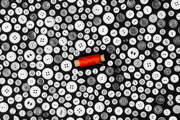 background - light buttons on a dark surface and reel of red thread with needle