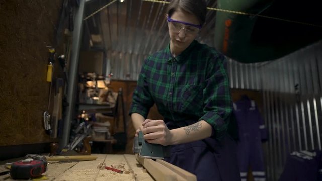 Young attractive woman joiner working with electric wood plane. Gender equality