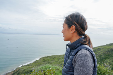 Young sporty Asian woman looking out at the beautiful ocean view. Young woman hiker standing admiring the view. healthy active lifestyle concept