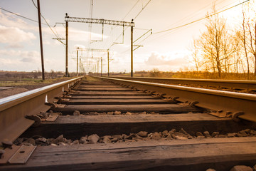 Fototapeta na wymiar Railway with rails on wooden sleepers on the background of a cloudy blue spring sky. Long road concept