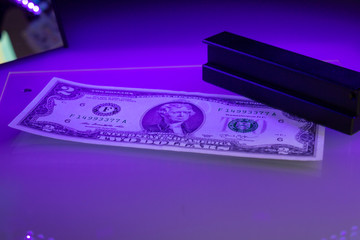 Verifying the authenticity of the two-dollar bill in ultraviolet light. US banknotes. Thomas...