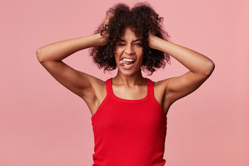 Joyful naughty african american girl with afro hairstyle playfully holds her hands to her head, has...