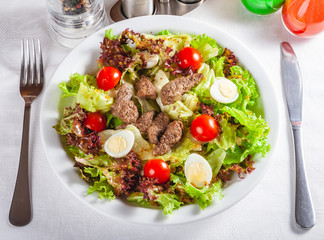Warm salad with chicken liver, tomatoes and eggs on white plate. Close up