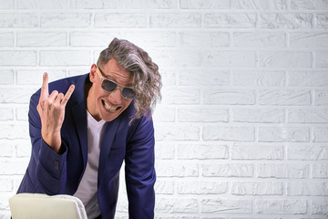 stylish businessman with curly long hair in sunglasses sitting on chair on white background