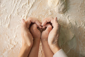 Mom and daughter make a heart with their hands while preparing the dough. Top view