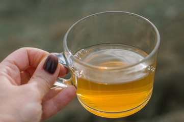 Green tea in a glass Cup in the hand of a girl with a manicure in a Burgundy sweater against the sea.