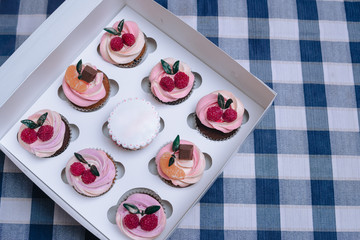 Closeup of colorful cupcakes decorated with sprinkles and strawberries in paper box, on blue table, copy space, composition with raspberry berries and green leaves, tangerine and chocolate