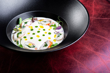 Cream soup is steaming in a black plate with on the black table. Photo for menu
