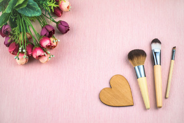 Obraz na płótnie Canvas Makeup brushes and flowers on pink background.