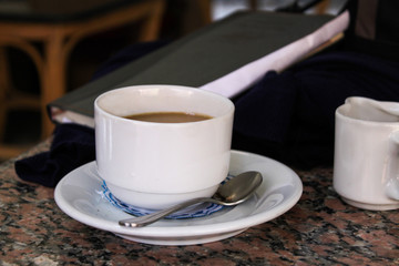 Fototapeta na wymiar White small cup with coffee on a saucer on the table, with a notepad in the background