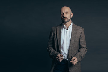 Serious middle aged man with a deadpan face expression dressed in casual posing on a dark gray background