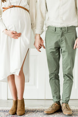 Young beautiful pregnant woman and her husband in hat standing near white wall