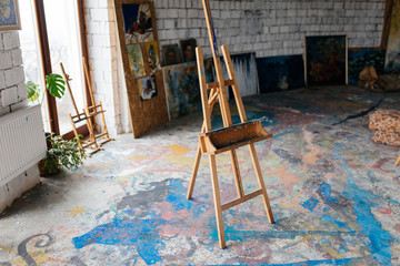 Close up photo of classic wood easel in modern cozy art workshop with colorful floor and window on background