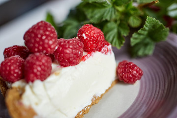 Slice of a fresh cheesecake with raspberries and mint