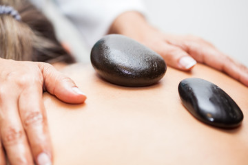 Doctor performing a hot volcanic stones therapy on a young female patient back