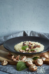 Mushroom risotto with spinach in a black plate on a gray background