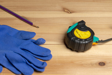 tape measure, protective blue gloves and a pencil on a piece of wood