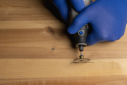carpenter in blue protective gloves handles wooden dremel