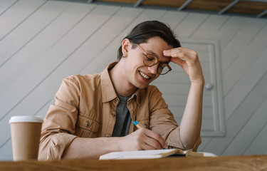 Handsome man working freelance project, planning strategy, looking creative solution, brainstorming. Happy student studying, taking notes in notebook, learning language, reading. Education concept