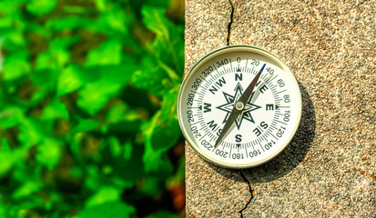 compass on gravel stone in strong sunlight with blurred natural green background, flat top view