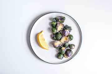 Healthy food concept, dieting, vegetarian, vegan - organic purple brussel sprouts fried on plate with lemon, top view