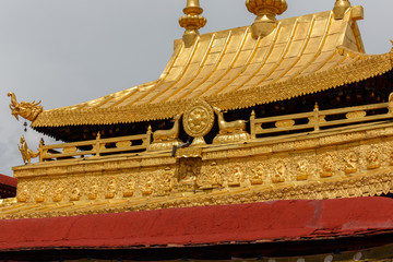 Fototapeta na wymiar LHASA, TIBET / CHINA - July 30, 2017: Close up of the rooftop of Jokhang Temple. In the middle the famous dharma wheel and deers. At the bottom part small buddha statues. Buddhist art, sculptures.