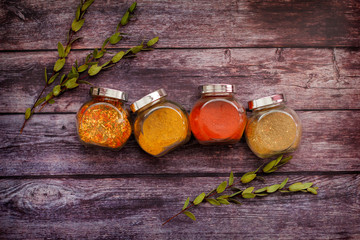 Glass jars with different colored spices and bay leaves on a wooden background