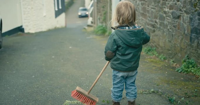 Little toddler standing in the street with a broom