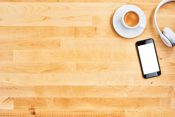 Smartphone with blank white screen, wireless headphone and cup of coffee on wooden office desk. Top view. Copy space for text or design. Flat lay.