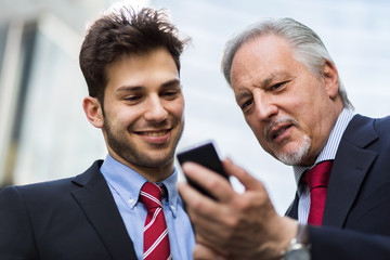 Senior manager showing something on a smartphone to his younger colleague