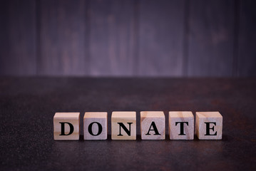 Fototapeta na wymiar The word donate on wooden cubes, on a dark background, symbols signs