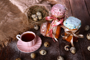 Three cakes or muffins with different icing and a cup of pink tea on a wooden background. Easter holiday concept. Still life concept.