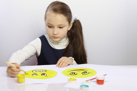 development of emotional intelligence. Girl draws a sad face and a cheerful yellow paint on paper. the development of empathy in a child