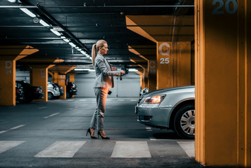 Elegant businesswoman with car keys in front of a car in underground parking. - obrazy, fototapety, plakaty