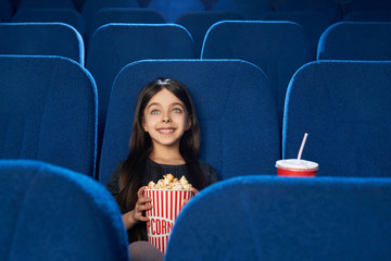 Beautiful, happy girl watching movie with popcorn in cinema.
