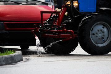 Obraz premium tractor with a barrel on a trailer pours water over the city sidewalks, streams of water flow down to the ground.