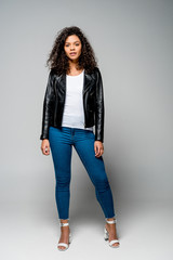 pretty african american girl in jeans and black jacket standing on grey