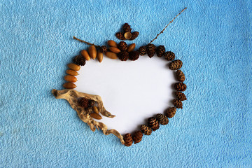 original frame in the form of a heart made of paper, small wooden block, acorns and cones on a blue...