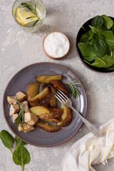 Baked potatoes sliced ​​with chicken fillet in a creamy sauce in a plate and salad bowl with spinach on a gray background top view.