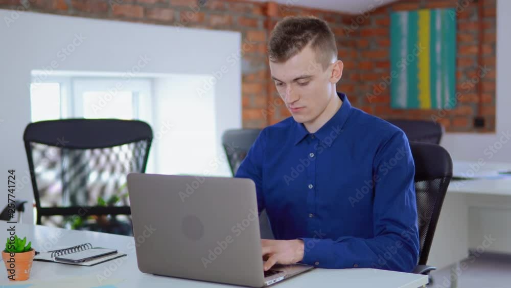 Poster young worker in startup company sitting at the white desk in loft office businessman focused looking