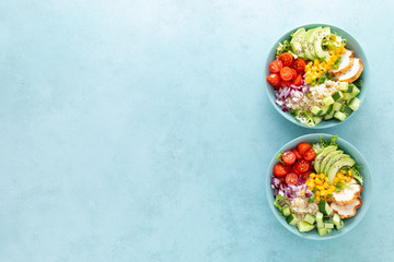 Lunch bowls with grilled cgicken meat, rice and fresh salad of avocado, cucumbers, corn, tomato and onion