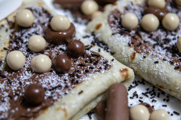 Homemade pancakes with chocolate, chocolate crumbs and candies on white plate