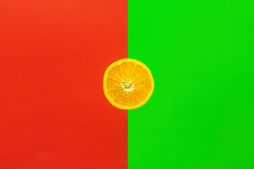 Orangenscheibe, halb aufgeschnittene Orange vor farbigem Hintergrund halb in kräftigem rot und grün