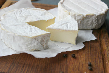 Camembert cheese. Farm products, rustic cheese. Natural cheese, round head of cheese with Camembert mold, cut on a wooden Board surrounded by fragrant spices. Cheese plate for gourmets.