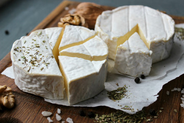 Camembert cheese. Farm products, rustic cheese. Natural cheese, round head of cheese with Camembert mold, cut on a wooden Board surrounded by fragrant spices. Cheese plate for gourmets.