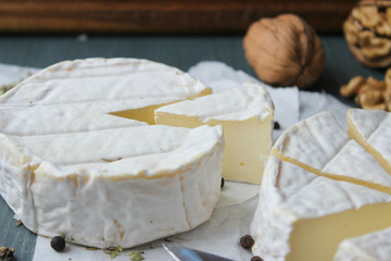 Camembert cheese. Farm products, rustic cheese. Natural cheese, round head of cheese with Camembert mold, cut on a wooden Board surrounded by fragrant spices. Cheese plate for gourmets.